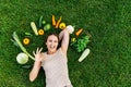 A woman lies on grass surrounded fresh vegetables