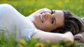 Woman lies on green grass, relaxing outdoors looking happy and smiling