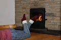 Woman lies near a burning fireplace and dangles legs in front of a fire, winter mood concept