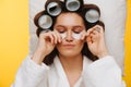 Woman lies on pillow with hair in rollers pressing patches under eyes to cheeks Royalty Free Stock Photo