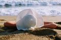 The woman lies on the sand against the background of the sea surf in a white hat with wide brim Royalty Free Stock Photo