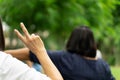 Woman lifts hand up and show two fingers of her hand in the garden, blur another people in background