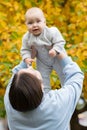 Woman lifts up charmed baby clenching fist in autumn park