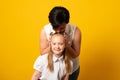 Woman in light clothes have fun with cute child baby girl. Mommy little kid daughter isolated on yellow background