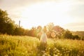 a woman in a light dress stands in a field in the warm rays of the setting sun holding a hat over her head Royalty Free Stock Photo