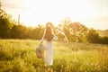 a woman in a light dress stands in a field in the warm rays of the setting sun holding a hat over her head Royalty Free Stock Photo