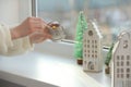 Woman lightning up candle near windowsill with house shaped lanterns indoors, closeup. Space for text