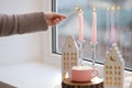 Woman lightning up candle near windowsill with house shaped lanterns indoors, closeup