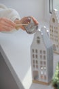 Woman lightning up candle near windowsill with house shaped lanterns indoors, closeup