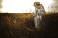 Woman in linen dress and hat walking in wildflowers and herbs in sunset golden light in summer meadow. Stylish rustic girl Royalty Free Stock Photo