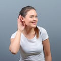 Woman listening with hand to ear concept against gray background Royalty Free Stock Photo