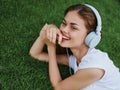 Woman listening to music with headphones in a white T-shirt on the green grass of the park lawn, meditating Royalty Free Stock Photo