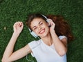 Woman listening to music with headphones in a white T-shirt on the green grass of the park lawn, meditating Royalty Free Stock Photo