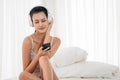 Woman listening to musics from smartphone and sitting on a bed in bedroom Royalty Free Stock Photo