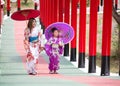 Woman and little girl in kimono holding umbrella walking into at the shrine red gate, in Japanese garden Royalty Free Stock Photo