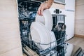 Woman loading the dishwasher. Open dishwasher with clean glasses and dishes close-up after washing