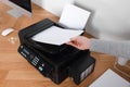 Woman loading paper into printer at wooden table indoors, closeup