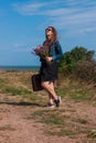 Woman with long brown hair in denim jacket, black skirt, vintage suitcase, flowers bouquet off-road. Lifestyle photo Royalty Free Stock Photo