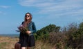 Woman with long brown hair in denim jacket, black skirt, vintage suitcase, flowers bouquet off-road. Lifestyle photo Royalty Free Stock Photo