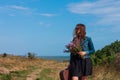 Woman with long brown hair in denim jacket, black skirt, vintage suitcase, flowers bouquet off-road. Lifestyle photo Royalty Free Stock Photo