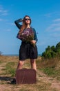 Woman with long brown hair in denim jacket, black skirt, vintage suitcase, flowers bouquet off-road. Lifestyle photo Royalty Free Stock Photo