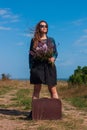 Woman with long brown hair in denim jacket, black skirt, vintage suitcase, flowers bouquet off-road. Lifestyle photo Royalty Free Stock Photo