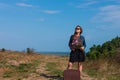 Woman with long brown hair in denim jacket, black skirt, vintage suitcase, flowers bouquet off-road. Lifestyle photo Royalty Free Stock Photo