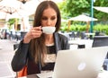 Woman with long brown hair, drinking coffee or tea, using her laptop on a restaurant`s terrace. Concepts of online shopping, Royalty Free Stock Photo