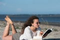 Woman with long curly hair reading a book at the beach