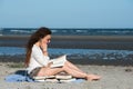 Woman with long curly hair reading a book at the beach