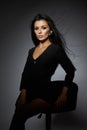 woman with long dark hair sits elegantly on a stool in a studio. lighting accentuates her features, creating a dramatic atmosphere Royalty Free Stock Photo