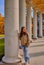 Woman with long hair in casual autumn wear is standing in gallery with columns. Walk in the park on a sunny day