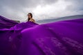 A woman with long hair is standing in a purple flowing dress with a flowing fabric. On the mountain against the Royalty Free Stock Photo