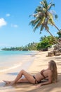 A woman with long hair in a swimsuit lies on the beach on the seashore with coconut palms. Rest and relaxation in Royalty Free Stock Photo