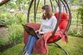 Woman with long hair typing at a laptop while sitting in a nest chair