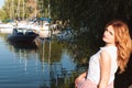 Woman with long hair in white blouse sitting near river with boats and looking at camera in yachts club Royalty Free Stock Photo