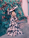 A woman in a long pink dress and a hat stands with her back to the camera