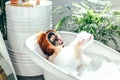 Woman with long red hair lying in bathtub with a clay mask on her face