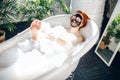 Woman with long red hair lying in bathtub with a clay mask on her face