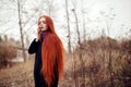 Woman with long red hair walks in autumn on the street. Mysterious dreamy look and the image of the girl. Redhead woman walking Royalty Free Stock Photo