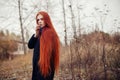 Woman with long red hair walks in autumn on the street. Mysterious dreamy look and the image of the girl. Redhead woman walking Royalty Free Stock Photo