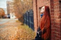 Woman with long red hair walks in autumn on the street. Mysterious dreamy look and the image of the girl. Redhead woman walking