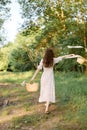 a woman in a long summer dress walks along a forest path holding a wicker hat with flowing ribbons in her hands Royalty Free Stock Photo