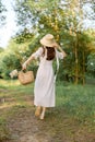 a woman in a long summer dress walks along a forest path holding a wicker hat on her head with her hand Royalty Free Stock Photo