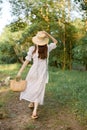 a woman in a long summer dress walks along a forest path holding a wicker hat on her head with her hand Royalty Free Stock Photo