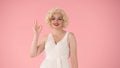 Woman in the look of Marilyn Monroe shows a gesture of ok. Woman with red lipstick on lips, wearing wig and white dress Royalty Free Stock Photo
