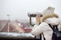 Woman looking through binoculars to the view of Tallinn Old Town on winter day. Romantic view of the snowy roofs of a medieval