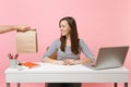 Woman looking on brown clear empty blank craft paper bag, work at desk with pc laptop isolated on pink background. Food