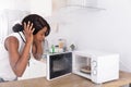 Woman Looking At Burnt Pizza In Microwave Oven