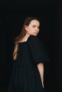 Woman looking at the camera over her shoulder. In black dress over black Royalty Free Stock Photo